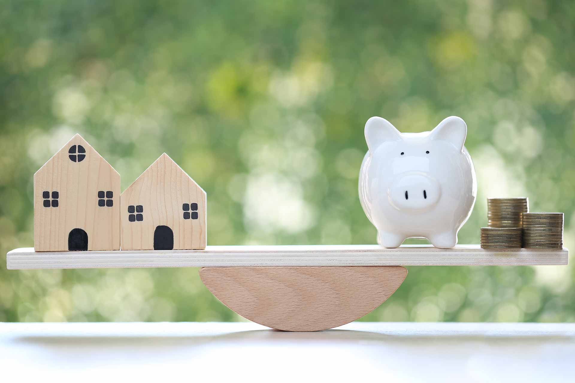 Modellhäuser, Sparschwein und Münzen auf einer Waage, Symbol für Immobilienpreise in Hürth