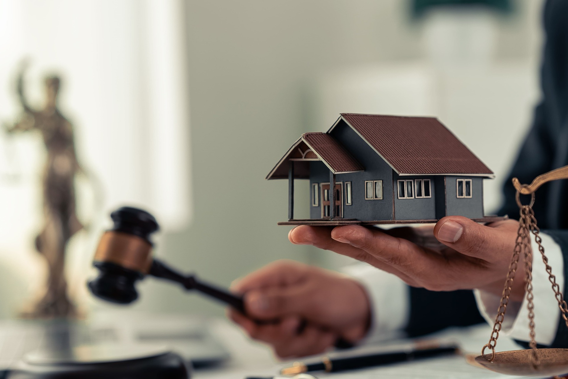 Eine Person hält ein Modellhaus in der Hand, in der anderen Hand einen Richterhammer