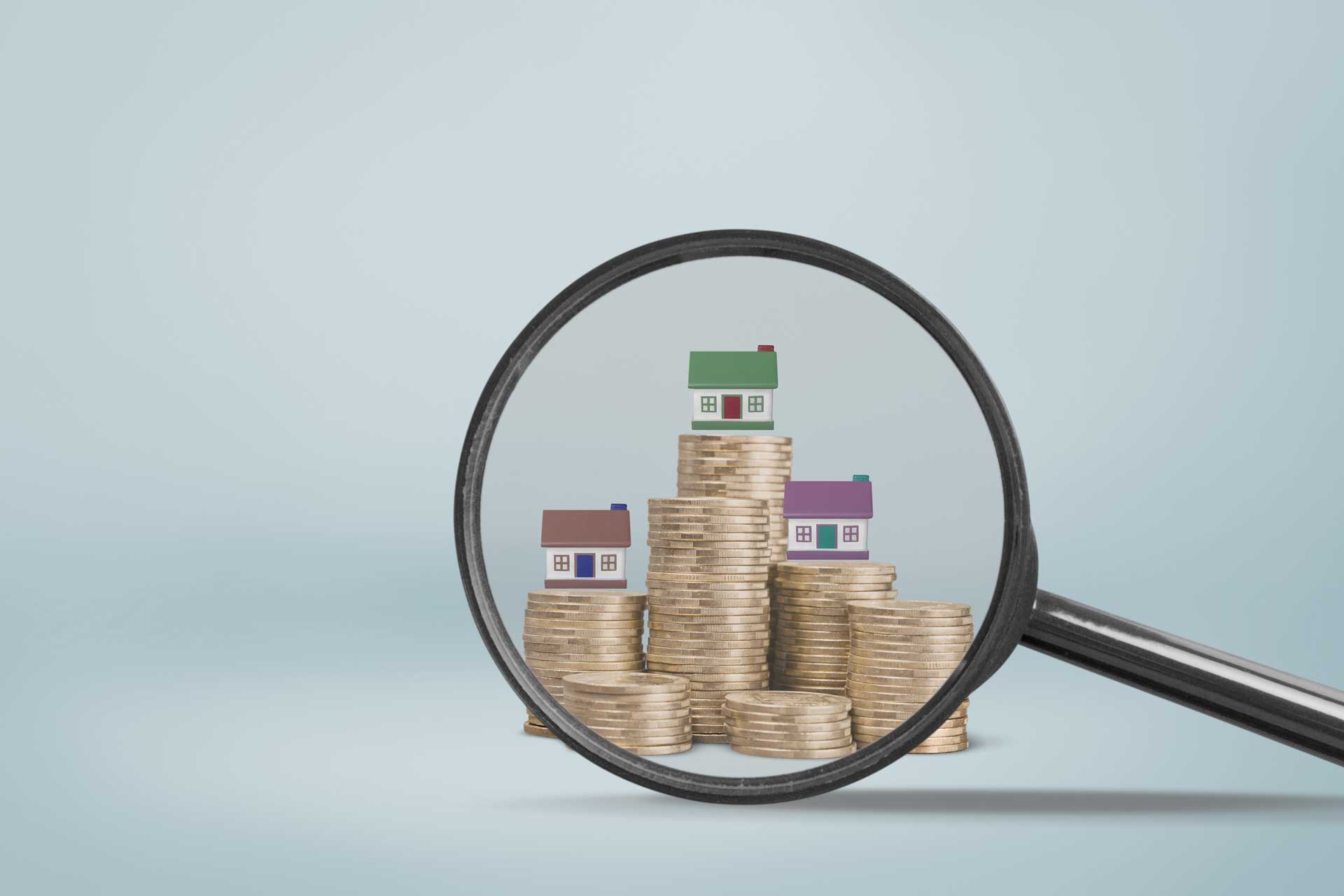 Lupe zeigt auf Miniaturhäuser auf Münzstapeln, symbolisiert Immobilienpreise Hürth