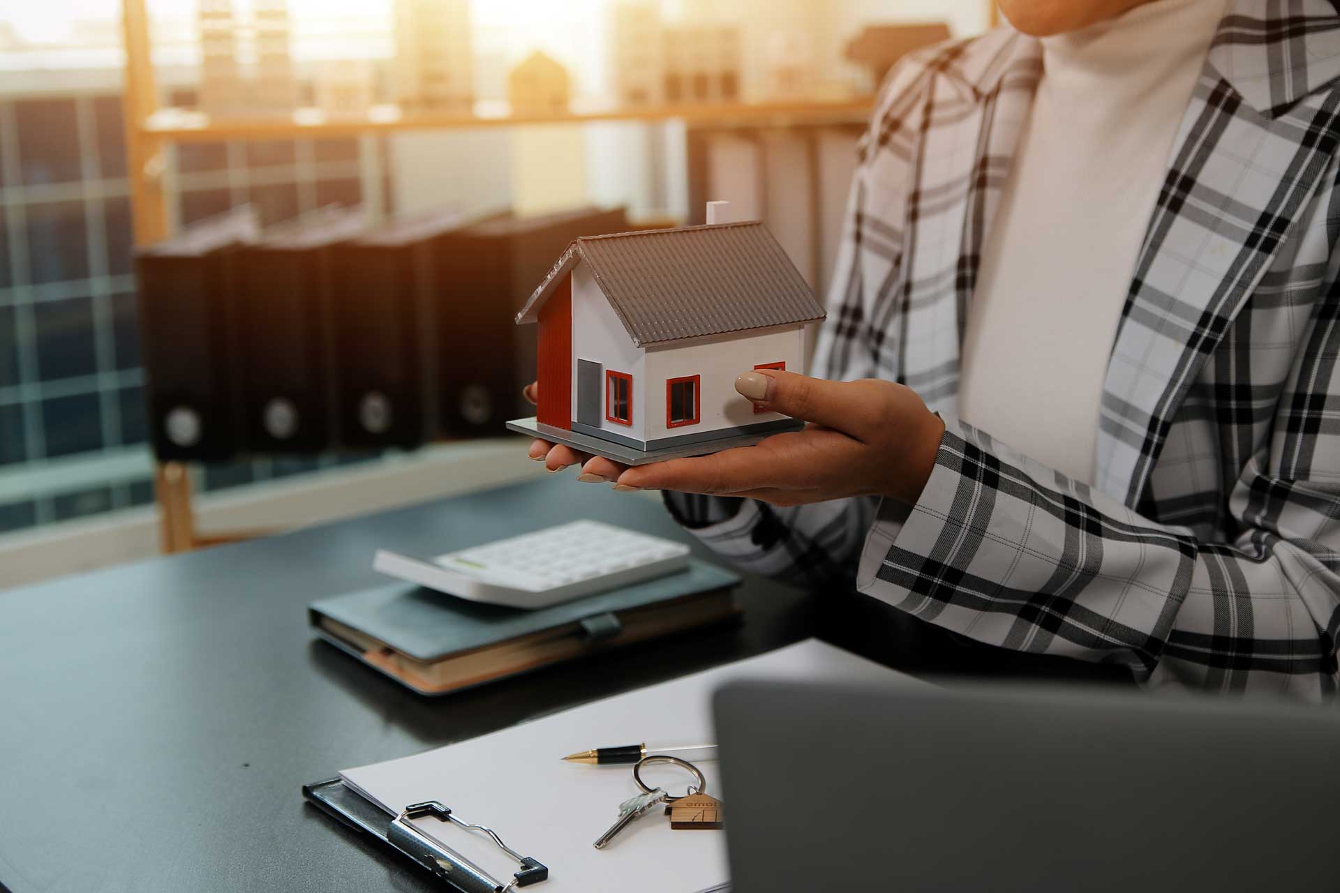 Maklerin hält Modellhaus in den Händen, symbolisiert Wertermittlung bei Erbschaft
